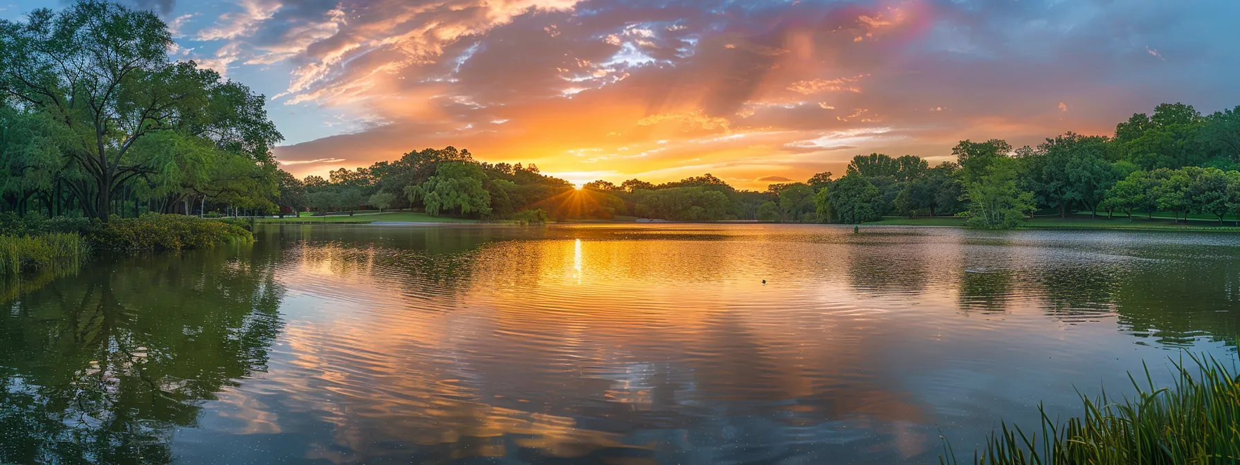 a vibrant sunset paints the sky in hues of orange and pink, reflecting beautifully on a tranquil lake surrounded by lush greenery.